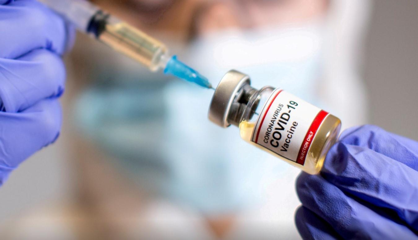 A woman holds a small bottle labeled with a "Coronavirus COVID-19 Vaccine" sticker - Avaz