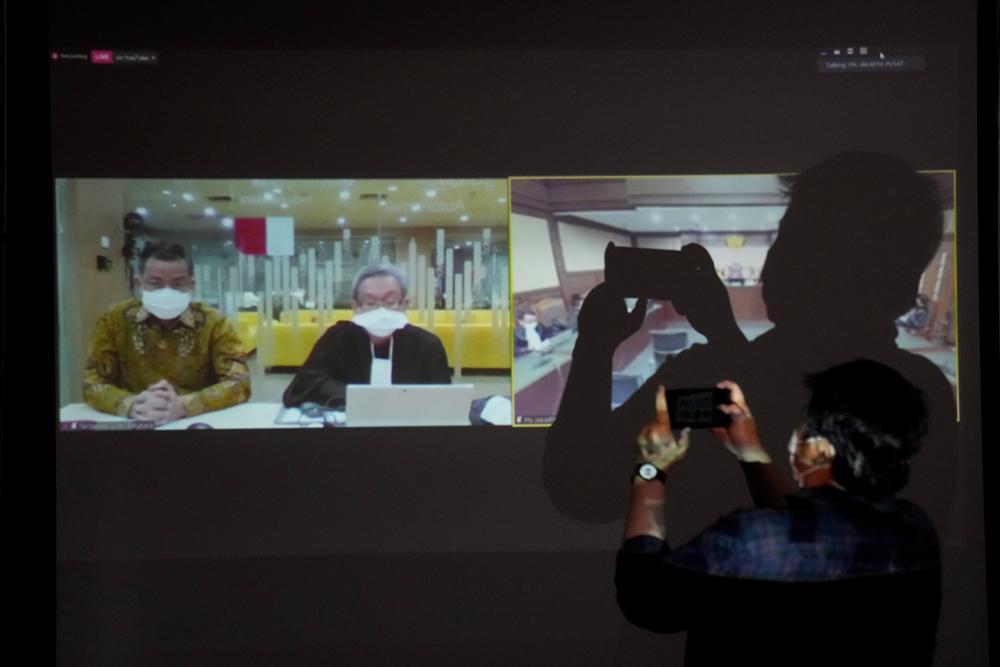 A journalist uses his mobile phone to take pictures of a large screen showing the live-streaming of the sentencing hearing of former Social Affairs Minister Juliari Peter Batubara, left, held virtually amid coronavirus outbreak, at the Corruption Eradication Commission building in Jakarta, Indonesia, Monday, Aug. 23, 2021. Indonesia's anti-graft court sentenced Batubara to 12 years in prison for his involvement in a bribery case pertaining to the government's COVID-19 aid distribution. - Avaz